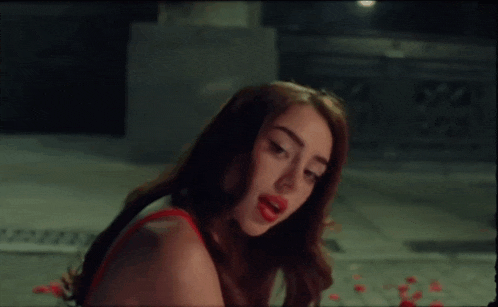 a woman in a red dress is standing in a dark room with red petals on the ground .