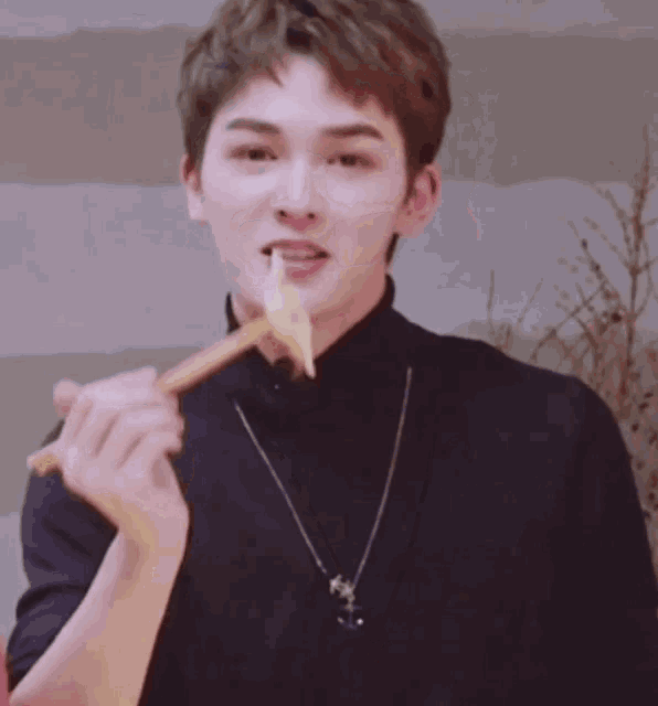 a young man in a black turtleneck is eating a piece of food
