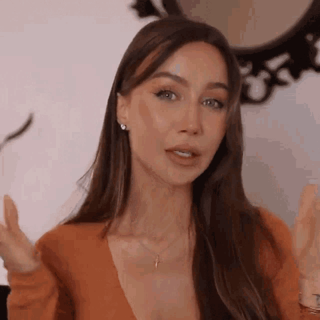 a woman with long brown hair is wearing a sweater and a necklace and making a funny face .
