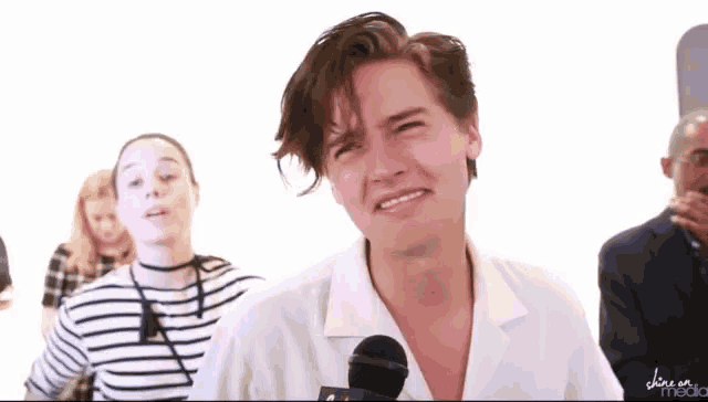 a man in a white shirt is making a funny face in front of a microphone with the word media on the bottom right