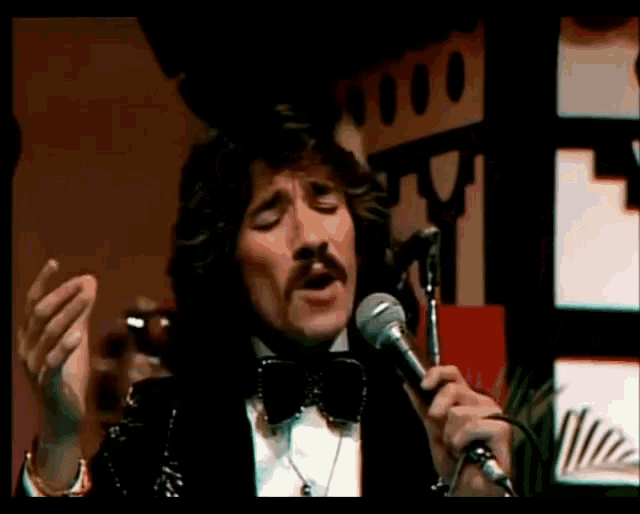 a man in a tuxedo singing into a microphone with his eyes closed