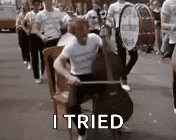 a man is sitting in a chair playing a cello in front of a marching band .