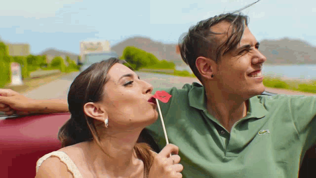 a man and a woman are sitting in a car and the woman is blowing a kiss at the man