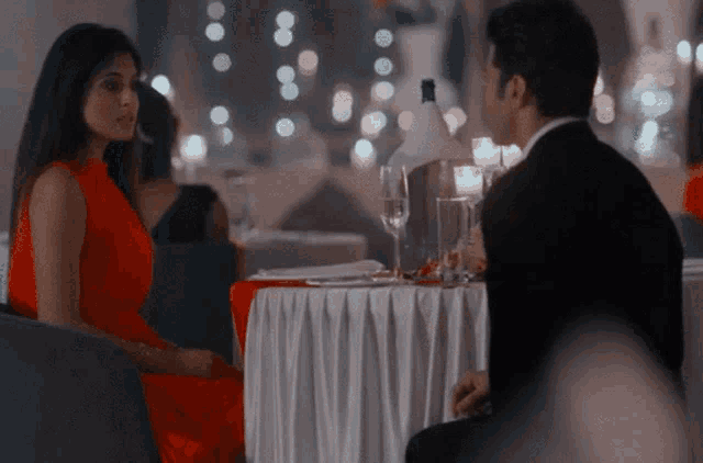a woman in a red dress sits next to a man in a suit at a table