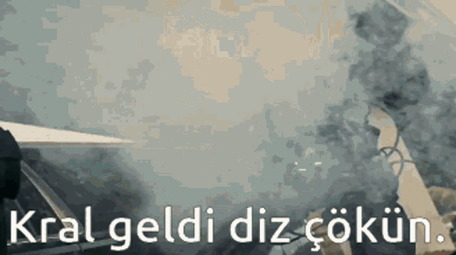 a man is driving a car with smoke coming out of the window and the words kral geldi diz cokun