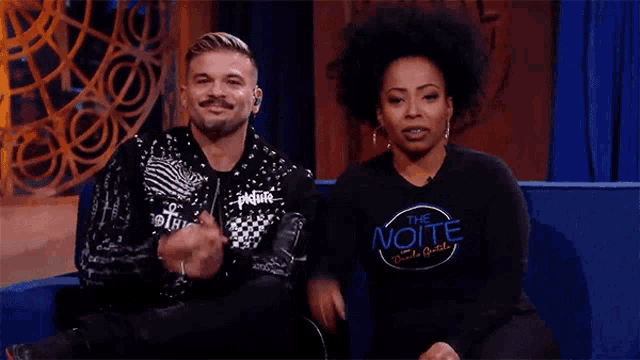 a man and a woman are sitting next to each other and the man is wearing a shirt that says ue noite