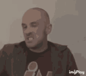 a bald man wearing a red shirt and a green jacket is making a funny face with his mouth open .