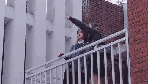 two girls standing on a balcony with one pointing