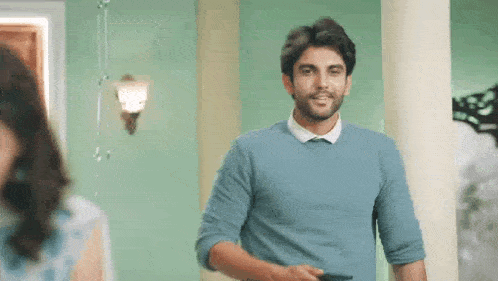 a man in a blue sweater and white shirt is standing next to a woman in a living room .