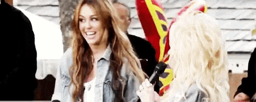 a woman is holding a microphone while another woman holds her hair .