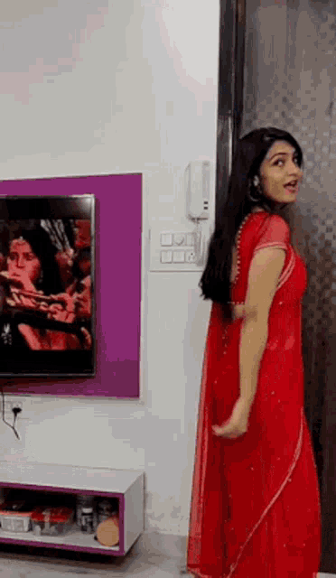 a woman in a red dress is dancing in front of a television .
