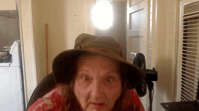 an elderly woman wearing a hat and a red shirt looks at the camera