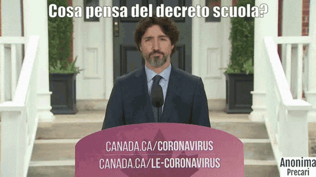 a man in a suit and tie stands at a podium with a sign that says canada.ca/coronavirus