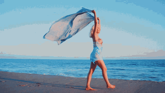 a woman in a white dress is dancing on the beach while holding a blue scarf