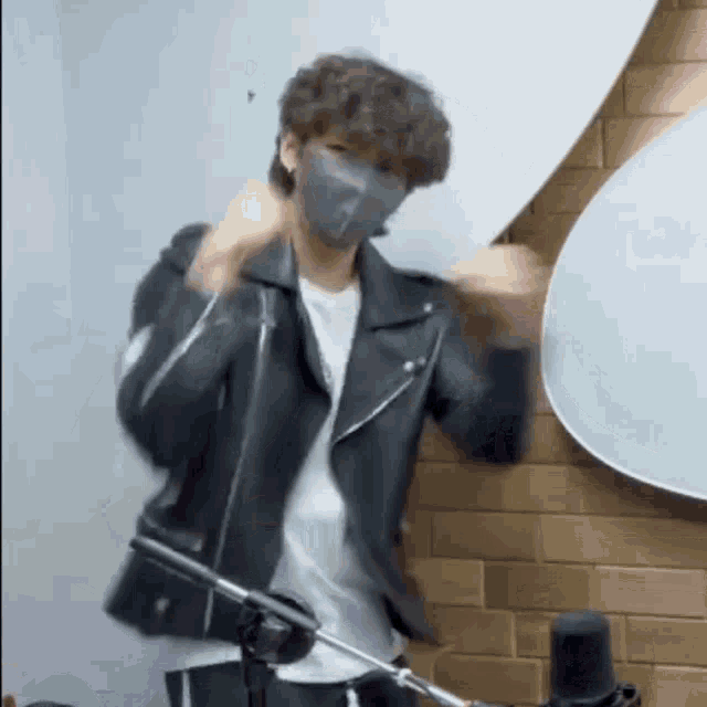 a man wearing a mask and a leather jacket is standing in front of a microphone in a room .