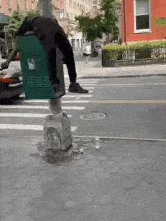 a person is standing on a green trash can on a street