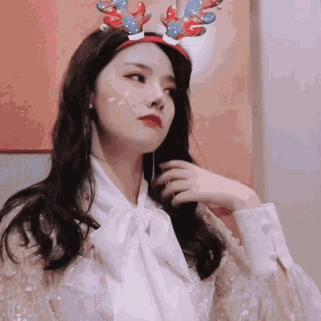 a woman wearing a headband with reindeer antlers looks at the camera