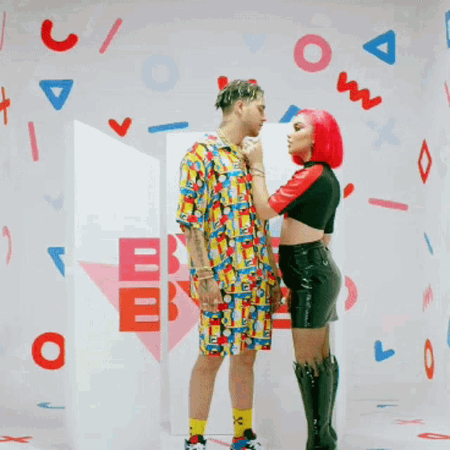 a man and a woman are standing in front of a wall with letters on it including the letter o