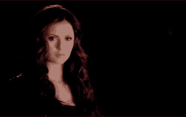 a woman with long dark hair is looking at the camera in a dark room