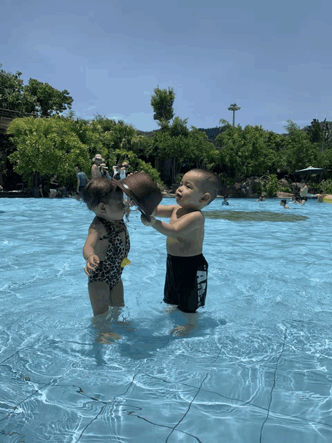 a boy and a girl are playing in a swimming pool with a bucket