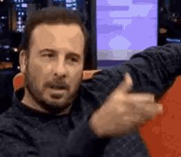 a man with a beard is sitting on a couch and making a funny face with his hands .