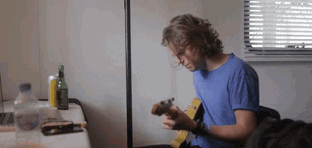 a man in a blue shirt is playing a guitar in a room