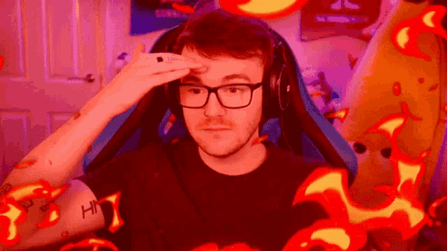 a man with glasses and headphones is sitting in a chair with flames around him .