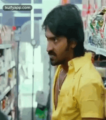a man in a yellow shirt is standing in front of a shelf in a store .