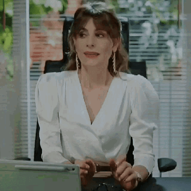 a woman in a white blouse is sitting at a desk with a laptop .