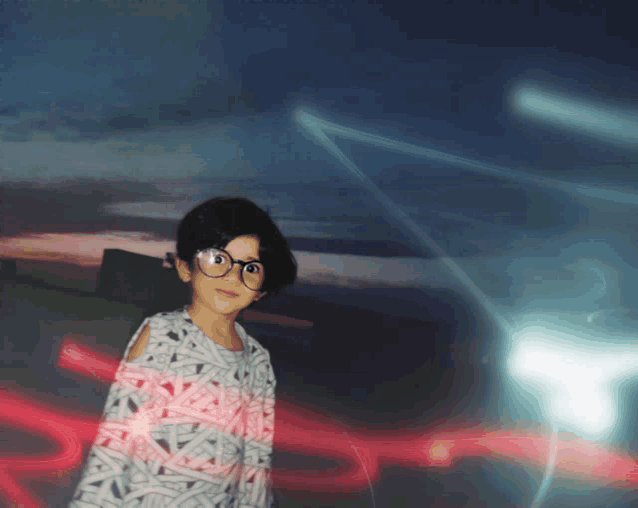 a little girl wearing glasses stands in front of a blurred background