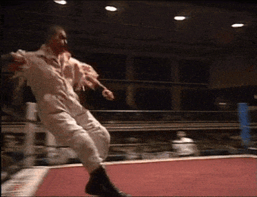 a man in a white jumpsuit is dancing in a boxing ring