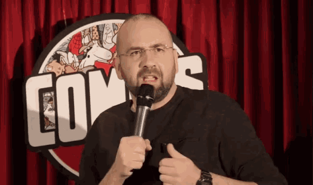 a man is holding a microphone in front of a sign that says comedy
