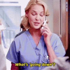 a woman in scrubs is talking on a cell phone and says what 's going down ?
