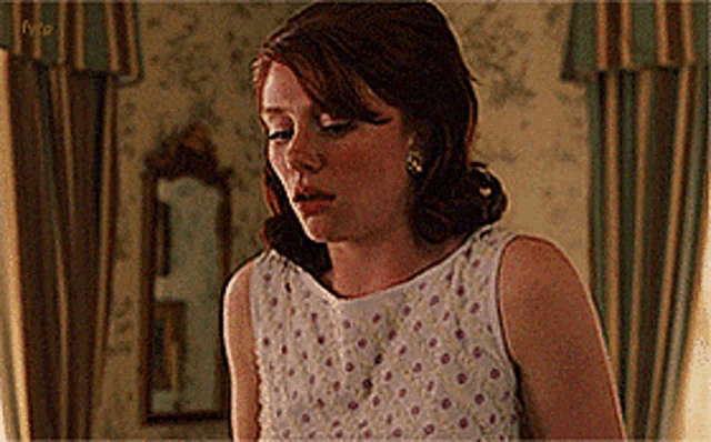 a woman in a white dress with pink polka dots is standing in a room