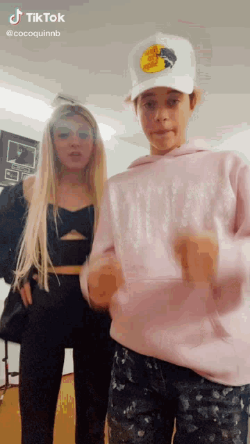 a girl in a pink hoodie is standing next to a boy in a white hat ..