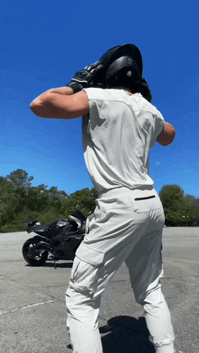 a man wearing a white shirt and white pants stands in front of a motorcycle