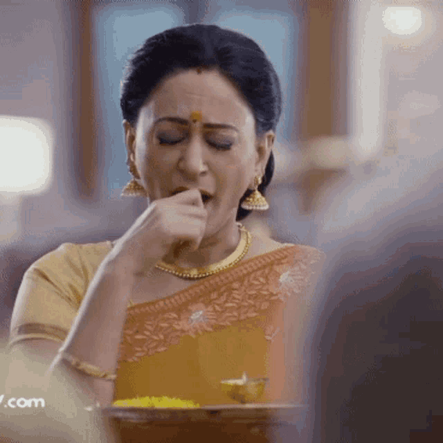 a woman in a sari is eating something with a .com watermark in the corner