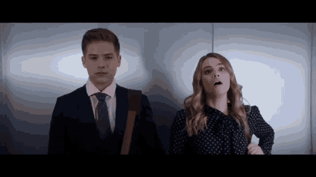 a man and a woman are standing next to each other in an elevator and looking up .