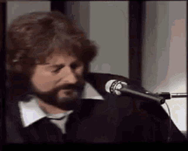 a man with a beard is singing into a microphone while wearing headphones .