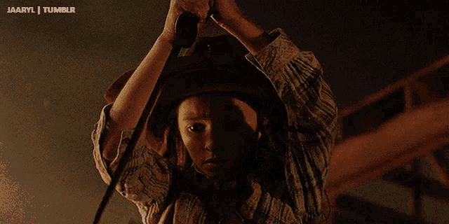 a person with a cowboy hat is holding a cane in a dark room with a tumblr logo behind them