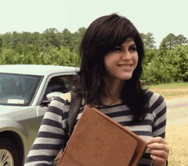 a woman in a striped shirt is smiling while holding a brown purse
