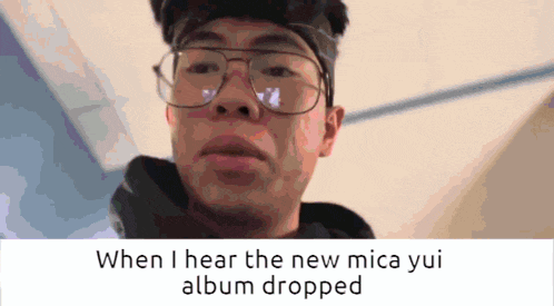 a man wearing glasses with the words when i hear the new mica yui album dropped below him