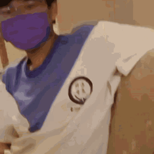 a man wearing a purple mask and a white shirt with a smiley face embroidered on it