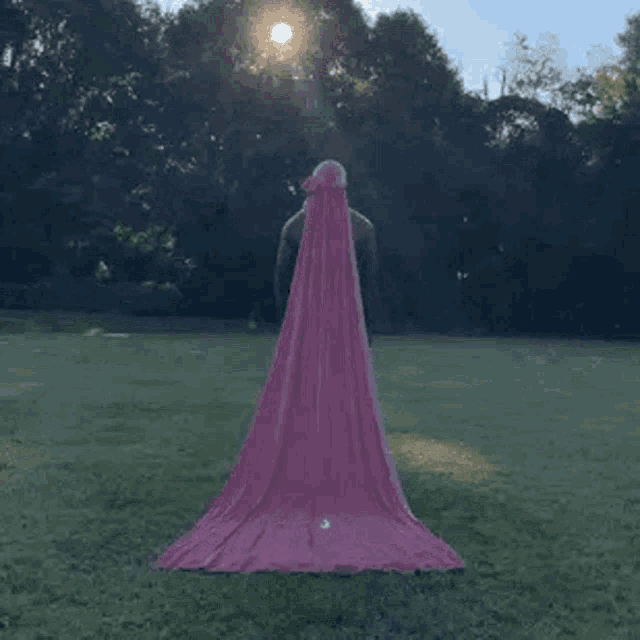 a man is standing in a field with a long pink cape .