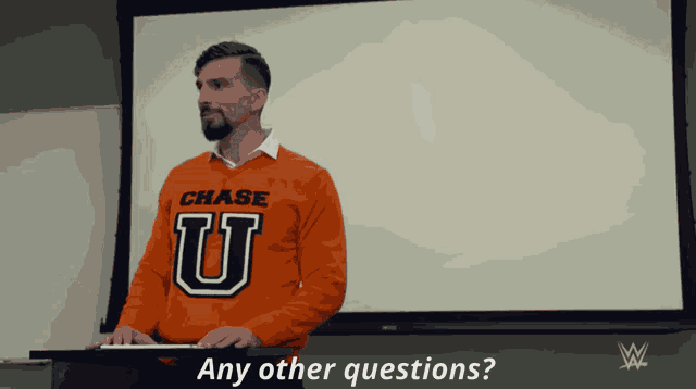 a man wearing an orange chase u sweater stands in front of a white board
