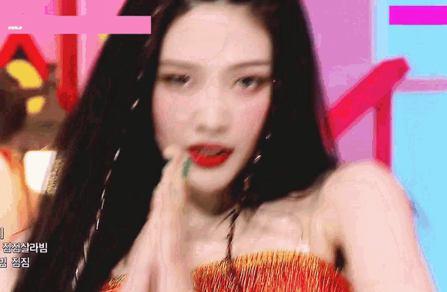 a close up of a woman 's face with a pink background . she is wearing a red dress and earrings .