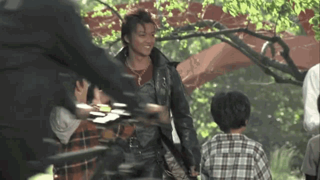 a man in a leather jacket is holding a child 's hand in a park .