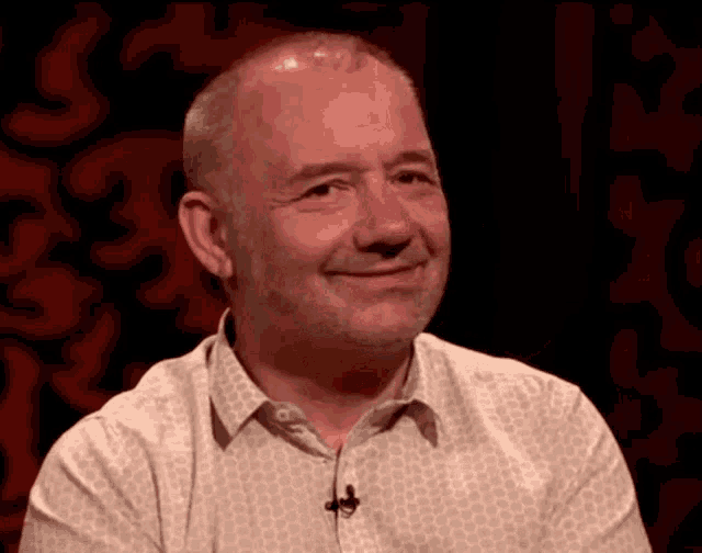 a man in a white shirt with a microphone on his neck smiles