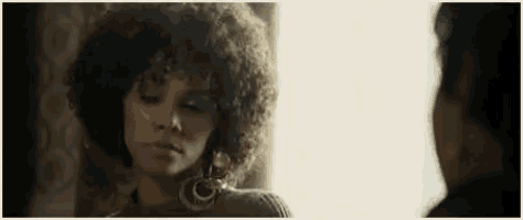a woman with curly hair is looking at a man with a serious look on her face