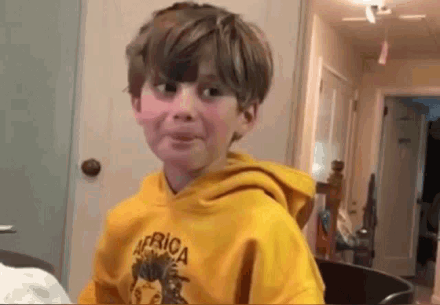 a young boy wearing a yellow africa sweatshirt making a funny face